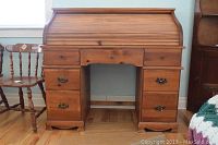 Front view of closed pine roll-top desk showing tambour top, drawer banks and center drawer