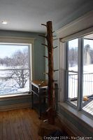 Full view of the tall coat tree positioned near corner windows, showing natural wood finish and many peg hooks