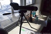 Black Daylight Monocular on small tripod placed on window ledge with some glass insulators in background.