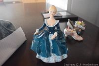 Figurine of seated woman in a blue dress on table showing full front.