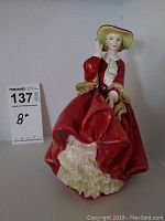 Front view of Royal Doulton figurine in red dress and yellow hat.