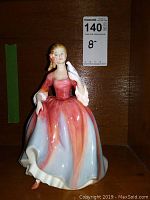 Full front view of Royal Doulton Nicola figurine standing against a wooden shelf background, showing the colorful glaze and white dove detail