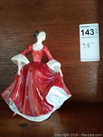 Front view of Royal Doulton Stephanie porcelain figurine wearing red gown, 7.5 inches tall, shown with auction tag.