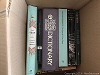 A box containing assorted books featuring The Nest, The New Collins Concise English Dictionary, Gone Girl, and others.