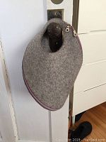 Large grey wool felt bag with pink zipper hanging from door knob, round cut handle