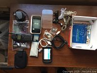 Photo showing Nokia 6160 phone, 8GB iPod, BlackBerry Torch with slide-out keyboard, accessories including manual, charging cables, earbuds, and phone case arranged on a table.