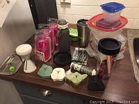 Photo of various kitchen items arranged on a counter including travel cups, food containers, spiralizer, tart pans, poach pods, and cookie cutters.