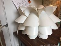 White Ikea hanging lamp with overlapping petal-like shade pieces on a wooden surface.