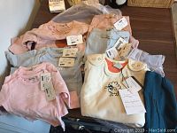 Photo showing seven long sleeve cotton shirts and three pairs of cotton pants arranged on a table with tags visible.