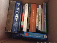 Books packed in a box showing titles like Rand McNally New World Atlas, dictionaries, and other hardcover reference books.