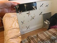 Showing the mirror being held up with starburst cutouts visible reflecting room décor and bedding.