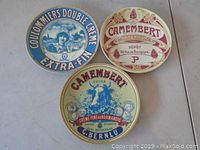 Three round metal decorative cheese tins with vintage product branding and advertising images