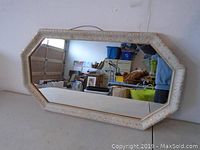 Front view of rectangular hanging wall mirror with beveled edges, textured cream-colored frame, and reflected background objects.
