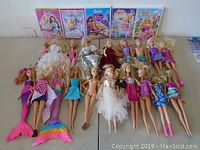 View of all Barbie dolls arranged on table showing varied outfits and conditions including a mermaid tail doll, wedding dress, casual and formal wear.