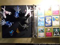 Photo of binder page showing Pokémon trading cards in sleeves and several Pokémon figurines placed nearby.