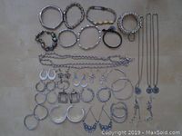 Overview photo showing assorted silver tone bracelets, earrings, necklaces, and chains laid out on a surface.