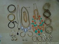 Full collection of assorted gold tone jewelry with mixed bracelets, necklaces, and earrings arranged on a surface.