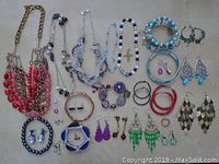 Full assortment of jewelry spread out on white background including necklaces, bracelets, earrings, and rings in various colors and styles.