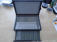 Jewelry box open showing top compartment with a removable insert including ring slots and divided storage areas, lined with gray velvet material.