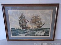 Frontal photo of the framed print showing two sailing ships on rough sea with cloudy sky, wooden frame, and beige matting.