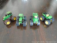 Four John Deere die cast toy tractors arranged in a line on a wood surface, showing size and tire variation