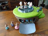 Photo of ceramic mouse house set on a wooden table showing house with green roof and three mice figurines on top