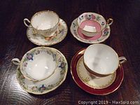 Four Aynsley bone china teacups on matching saucers set against a dark background, showing distinct floral and gold designs.