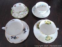 Four porcelain teacups with matching saucers, each featuring distinct floral patterns and gold trim, displayed on a dark surface.