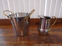 Front view of both stainless steel bucket and jug showing overall shape and brass handles.