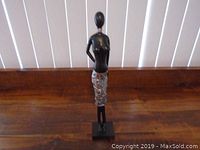 Front view of the wooden female figurine sculpture showing the black upper torso and the detailed silver skirt pattern.