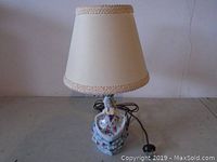 Vintage table lamp with floral ceramic base and beige fabric shade, shown powered off with the cord wrapped beside it