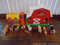 Wide view of the two plastic barns and eleven assorted toy farm animals in front of them.