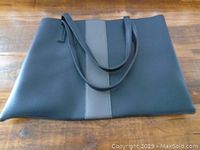 Full view of the Vince Camuto tote bag laid flat on wooden surface showing the front side with a large central gray vertical stripe and two handles.