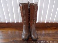 Front view of knee-high brown leather boots with leopard print fabric sides and decorative rivets along the top.