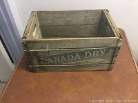 Front and side view of vintage wooden crate with Canada Dry branding on a table, showing weathered wood and paint.