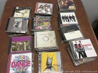 Photo showing multiple stacks of CDs including Train, Eurhythmics, Aaron Neville, and various compilations.