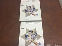 Photo showing two identical souvenir books from 1987 with Canada Post stamps on a brown surface, white cover with beige star detail and visible stamps inside.