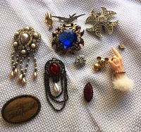 Full view of all 11 vintage brooches arranged on white cloth showing variety of styles and materials including pearls, rhinestones, enamel, and faux fur.