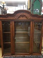 Front view of the cherry finish display hutch cabinet with glass center door and scroll wood design top.