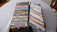Photo showing two stacks of assorted DVDs on a white tablecloth, titles visible for many cases.