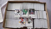 Photo of a large box filled with approximately 4,000 hockey cards in stacks with six sample cards on top showing different hockey players.