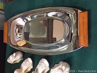 Stainless steel tray with rectangular Bakelite handles on a green surface with four white swan napkin ring holders below it.