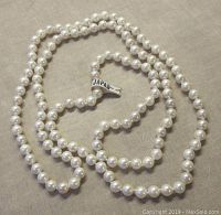 Photo showing the full length of the pearl necklace laid out coiled, highlighting the white glass pearls and the Japan paper label attached to the strand.