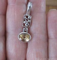 Front view of the sterling silver pendant showing the floral open work design and the faceted oval citrine colored stone.