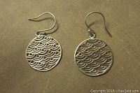 Pair of sterling silver open work dangling earrings laid on fabric showing front design with wave pattern.