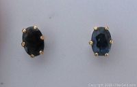Close-up of the two oval sapphire stud earrings showing the gold prongs and stone color difference.
