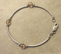 Photo of a delicate sterling silver bracelet showing curved silver tubes, small silver beads, and three citrine-colored faceted glass beads, with lobster clasp marked 925.