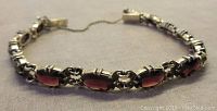 Full view of gold plated link bracelet displaying garnet-coloured oval stones and safety chain.