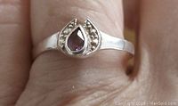 Close-up photo of sterling silver ring worn on a finger showing small teardrop amethyst stone bezel set at the top