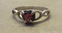 Close-up view of the ring showing the heart-shaped garnet coloured stone and the prong setting on the ring's band.